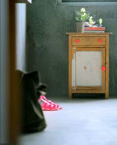 a small wooden cabinet sitting in front of a green wall next to a pink flower pot