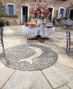 an outdoor dining area with tables, chairs and potted flowers on the table in front of a stone building