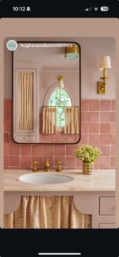 a bathroom with pink tile and gold accessories on the sink, along with a large mirror