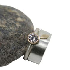 a pair of rings with a diamond sitting on top of a rock next to some rocks