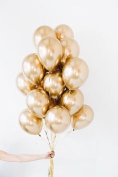 a woman holding a bunch of gold balloons