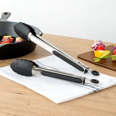 two tongs are sitting on top of a napkin near a skillet with food in it