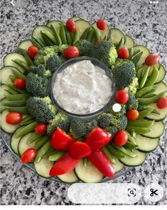 a platter filled with cucumbers, tomatoes, broccoli and dip