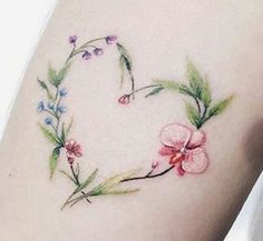 a heart shaped tattoo with flowers and leaves on the side of the arm, painted in watercolor