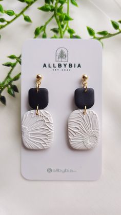 the black and white earrings are on display next to some green plant leaves in front of it