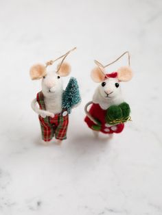 two mice dressed up in christmas clothes and holding a tree ornament on a white surface