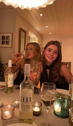 two women sitting at a dinner table with wine glasses in front of them and candles on the table