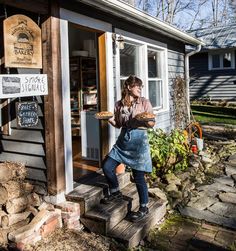 a woman standing on the steps outside of a store holding a tray of food in her hand