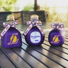 three small bottles are sitting on a wooden table, one is purple and the other is gold