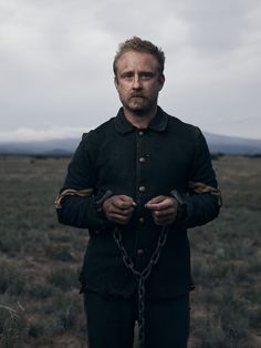 a man standing in the middle of a field with his hands wrapped around him and wearing chains