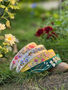 several colorful bowls sitting on the ground in front of some flowers and grass with rocks