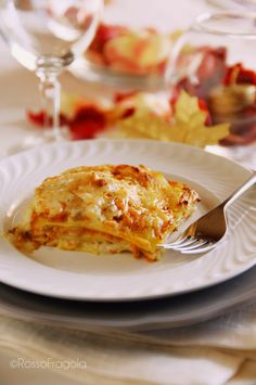 a white plate topped with lasagna next to a glass of wine and silverware