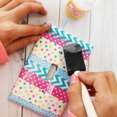 someone is painting a light switch cover with polka dot paper and paintbrushes on a white wooden table