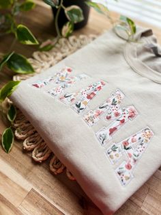 an embroidered t - shirt sitting on top of a wooden table next to some plants