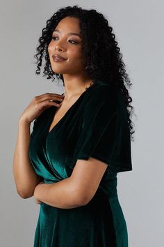 a woman with curly hair wearing a green dress and holding her hand on her shoulder