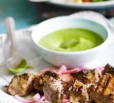 some meat and vegetables on a plate with a bowl of green sauce