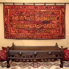 an antique bench is sitting in front of a large rug on the wall behind it