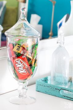 a glass jar filled with assorted candy on top of a white counter next to a mirror