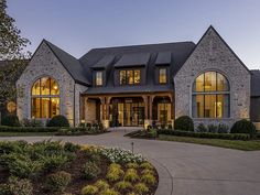 a large house with lots of windows and lights on it's front porch, surrounded by greenery