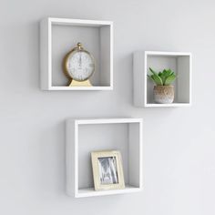 three square shelves with pictures and clocks on the wall next to each other in different colors