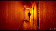 a person walking down a long hallway in an orange lit area with red lighting on the walls