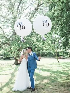 a bride and groom kissing under two balloons with the word mr and mrs written on them