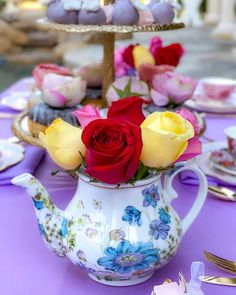 roses in a teapot on a table with plates and silver utensils for desserts