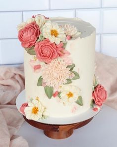 a white cake with pink and yellow flowers on it sitting on top of a wooden stand