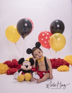 a little boy sitting in front of balloons and mickey mouse