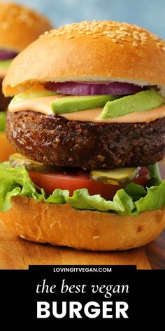 two hamburgers with lettuce, tomato and pickles on a cutting board