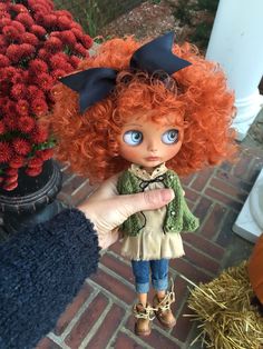 a doll with red hair and blue eyes is being held by someone's hand