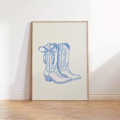 a blue and white drawing of cowboy boots in a frame on the floor next to a wall