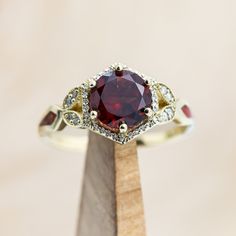 a ring with a large red stone surrounded by small white diamonds on a wooden stand