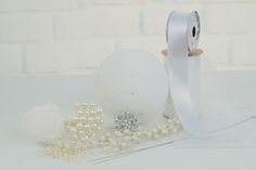 a roll of white satin ribbon next to pearls and other accessories on a table with a brick wall in the background