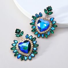 These Big Heart Halo Luxury Glass Formal Dangle Drop Statement Earrings boast a striking combination of vibrant crystal color and rhinestone inlay, creating an eye-catching heart design. The perfect addition to any formal outfit for an opulent and sophisticated look. Available in 5 different colors. Details Item Type: Fashion Earrings Metal Type: Zinc Alloy Material: Acrylic,Rhinestone Size: 6.1*4.9cm Back Finding: Push Back Glamorous Crystal Heart Earrings, Glamorous Rhinestone Heart Earrings For Party, Crystal Heart Drop Earrings For Party, Blue Heart Earrings For Party, Double Heart Rhinestone Jewelry For Party, Green Heart Shaped Earrings For Parties, Green Heart-shaped Jewelry For Party, Glamorous Heart-shaped Crystal Earrings, Green Heart Earrings For Valentine's Day Party