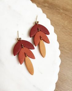 two pairs of red and orange earrings on top of a white plate with a wooden surface