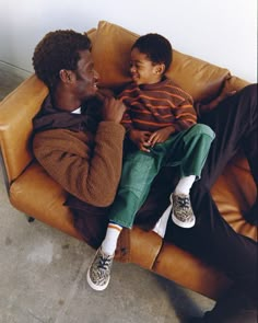 a man sitting on top of a brown couch next to a little boy in his lap