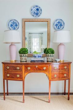 a table with two vases on top of it next to a mirror and lamp