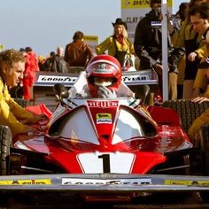 a man sitting in a racing car with other people around him