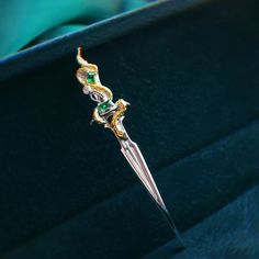 a green and gold brooch sitting on top of a blue velvet box with a metal handle