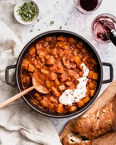 a pot filled with stew next to bread and wine