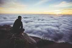 a man sitting on top of a mountain above the clouds