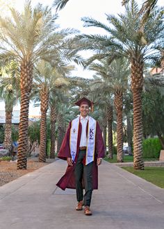 a man in graduation gown walking down a path with palm trees on either side of him