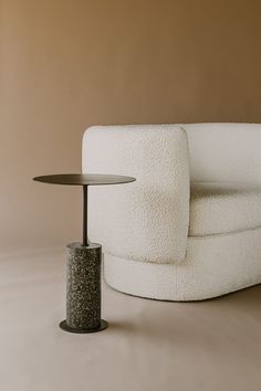 a white chair with a black table next to it on a gray floor and brown wall