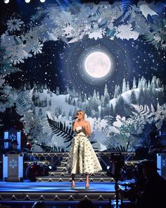 a woman standing on top of a stage in front of snow covered trees and stars