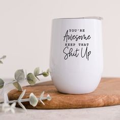 a white wine glass sitting on top of a wooden cutting board next to some leaves