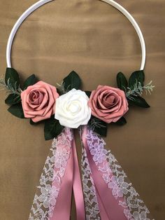 a white hoop with two pink roses and green leaves hanging from it's sides