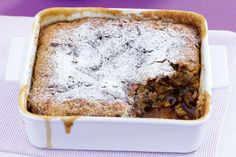 a casserole dish is covered with powdered sugar and chocolate sauce on a purple tablecloth