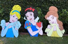 three cardboard cut outs of disney princesses in front of a hedge with bushes behind them