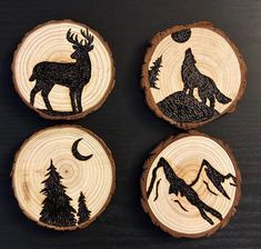 four wood burned coasters with animals and trees in the woods on them, each decorated with a silhouette of a wolf